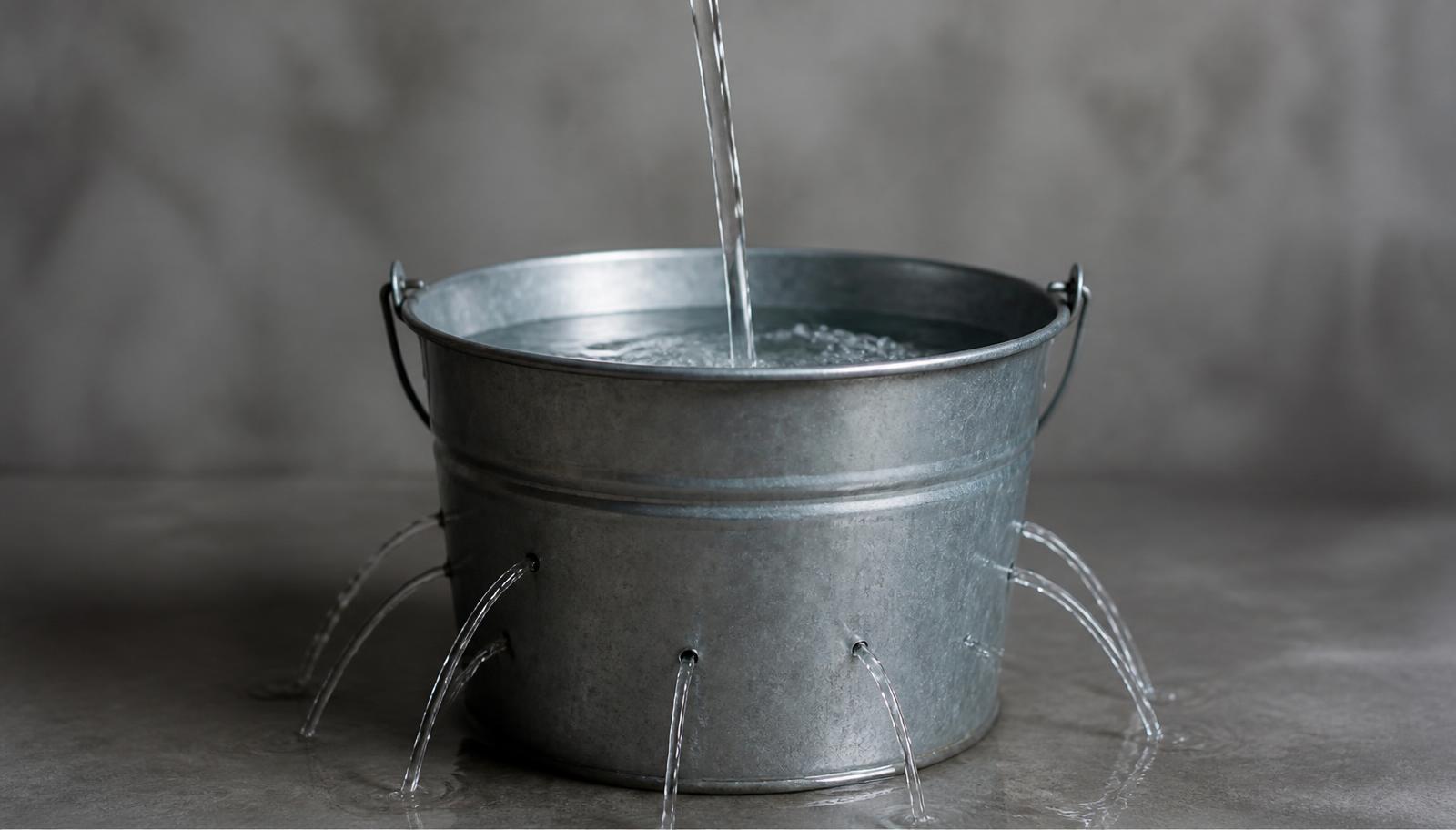 Cubeta metálica con agua entrando desde arriba mientras pequeños chorros escapan por orificios en sus paredes